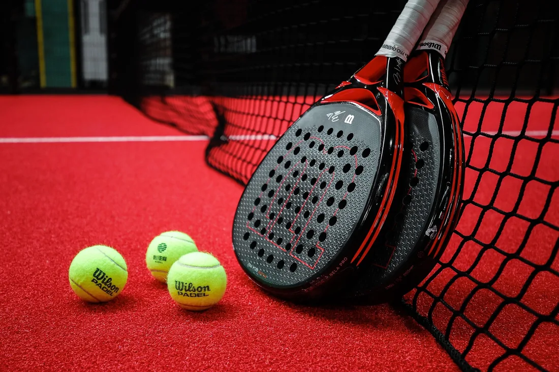 Padelschläger und Padelbälle auf einem roten Platz